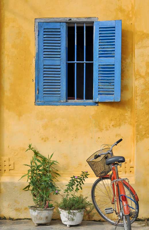 Blue shuttered window on yellow wall with bike outside in Hoi An