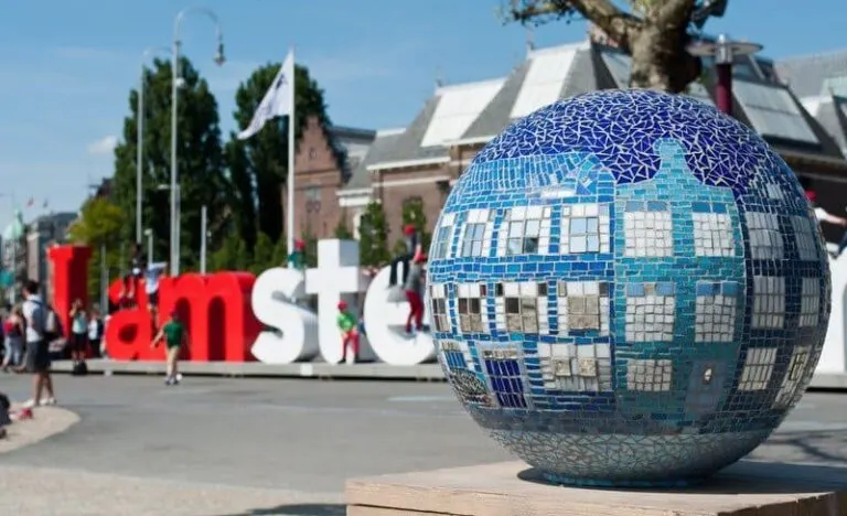 red and white I Amsterdam Sign with mosaic blue ball in the foreground with canal houses