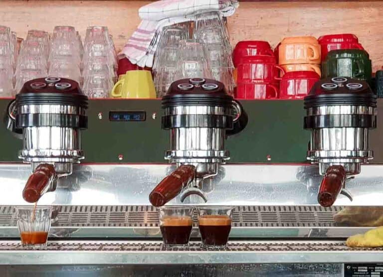 Coffee machine pouring espresso coffee with red yellow and orange coffee cups and espress glasses piled on top of it