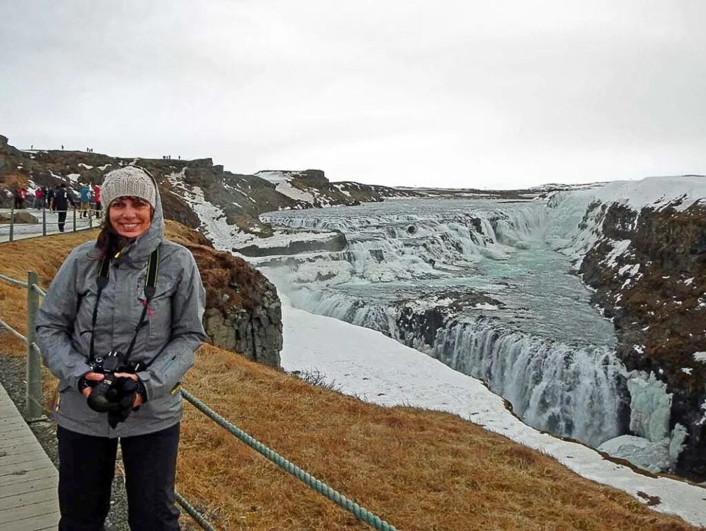 Woman wearing warm winter clothes standing by Gulfoss waterfall in Iceland
