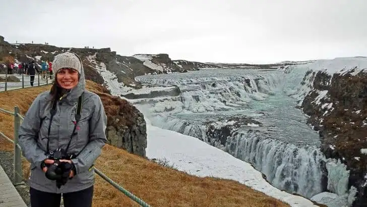 Woman wearing warm winter clothes standing by Gulfoss waterfall in Iceland