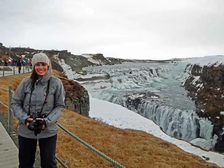 Woman wearing warm winter clothes standing by Gulfoss waterfall in Iceland