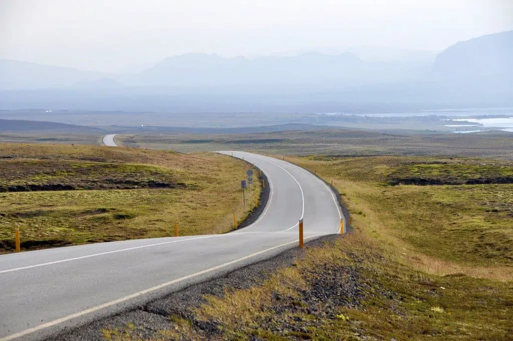 winding road in remote area of Iceland with grassland on each side and the vague outline of clouds in the distance