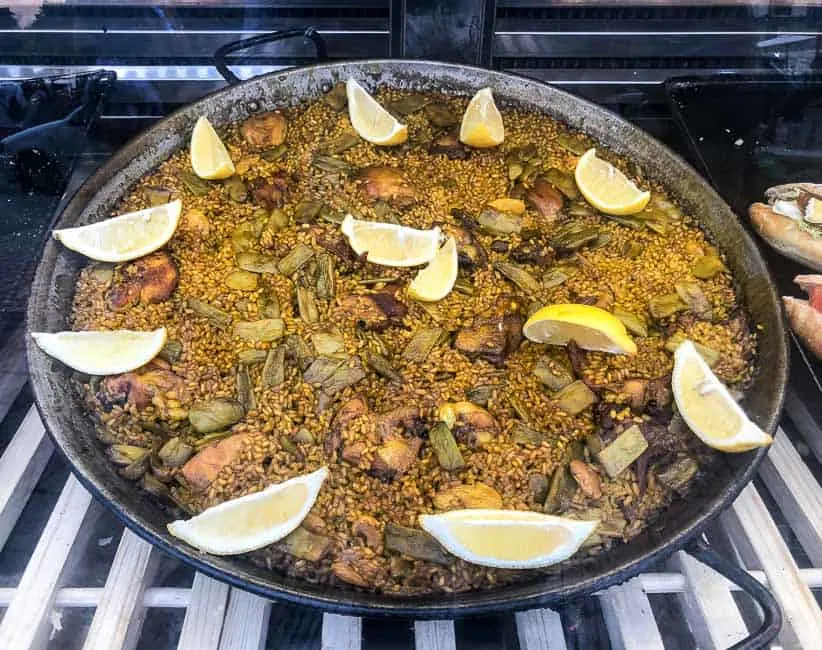 Valencian Paella in paella pan with lemon wedges