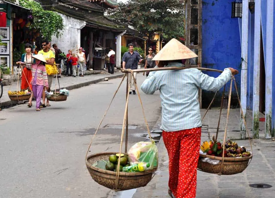 Vietnamese woman walking with baskets and non la hat