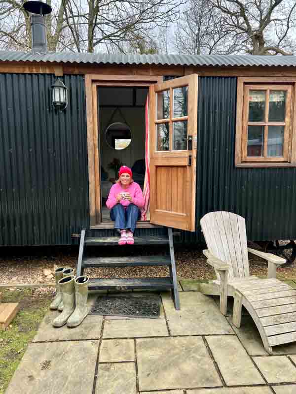 Woman in pink hat and pink top sitting on the shepherd hut steps