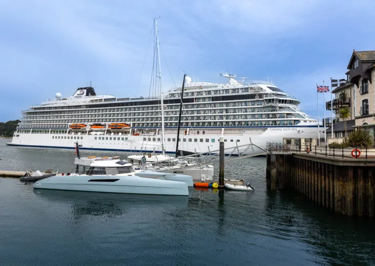 Viking Saturn in port a Falmouth. There are two small catamarans in the foreground and a building to the right.