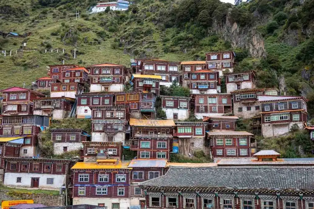 Wooden Tibetan houses with colorful roofs cascade down a green hillside.