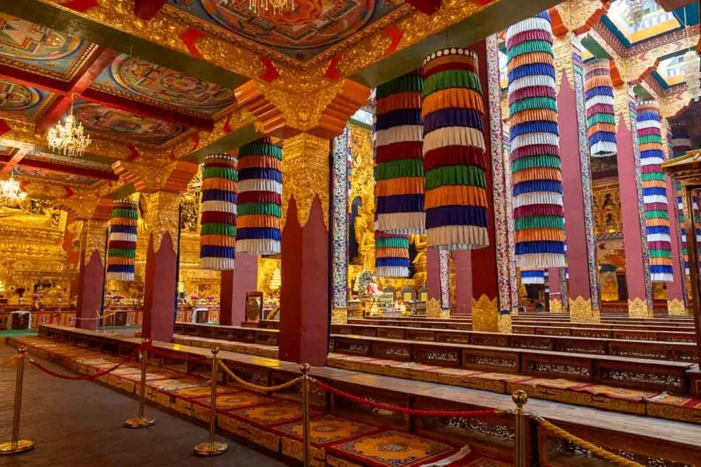 Ornate temple interior with colorful hanging decorations, red and gold pillars and rows of seating.