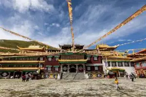 Tibetan monastery with prayer flags and people in a stone courtyard.