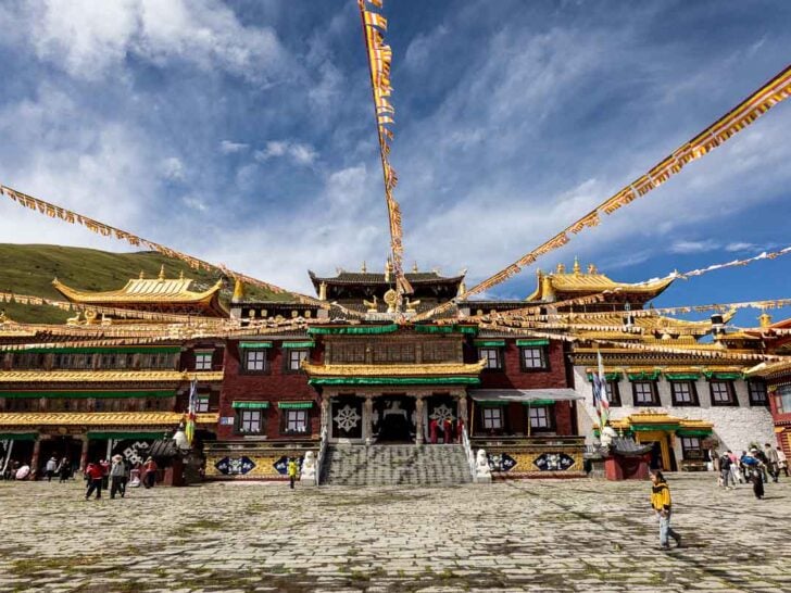 Tibetan monastery with prayer flags and people in a stone courtyard.