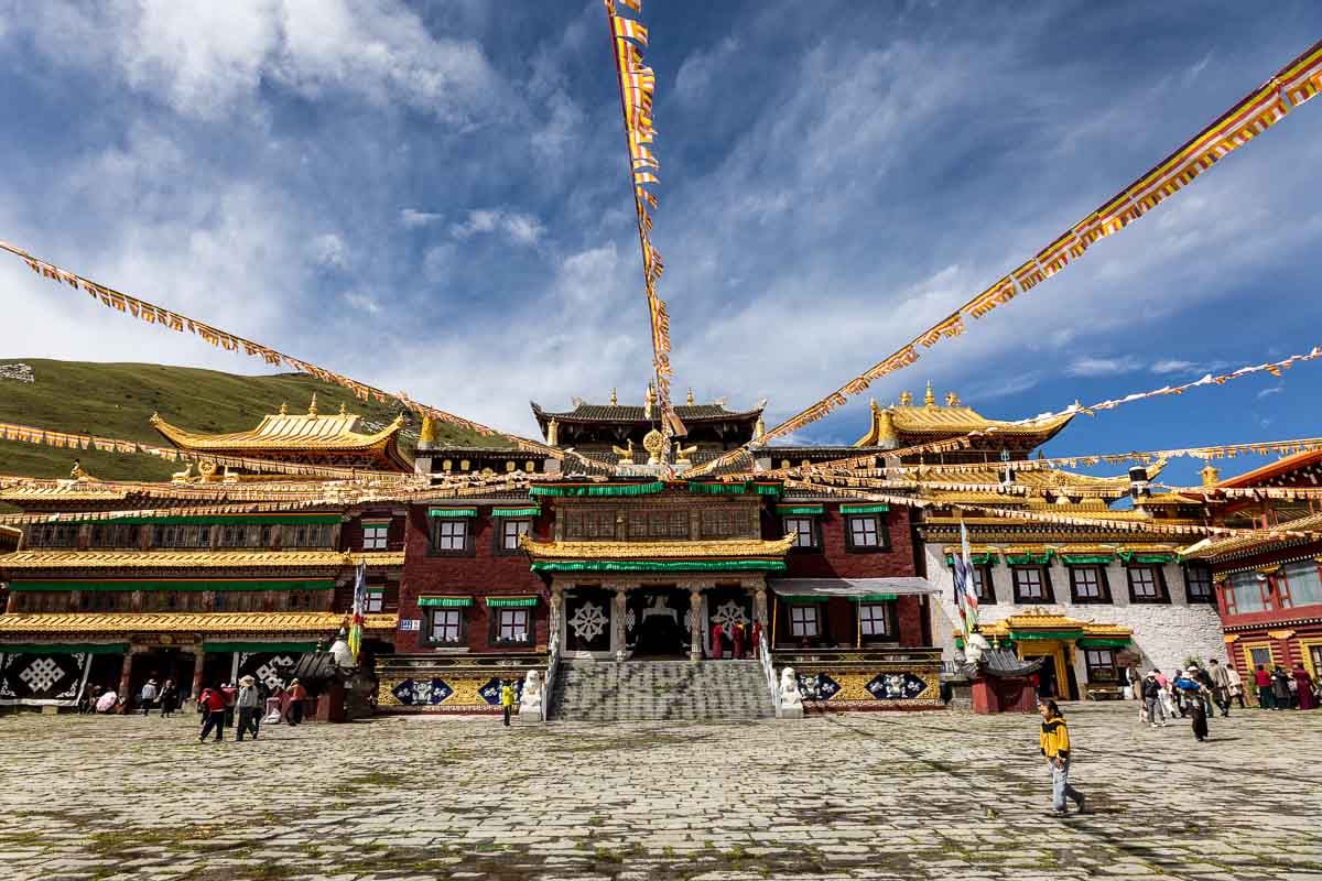 Tibetan monastery with prayer flags and people in a stone courtyard.