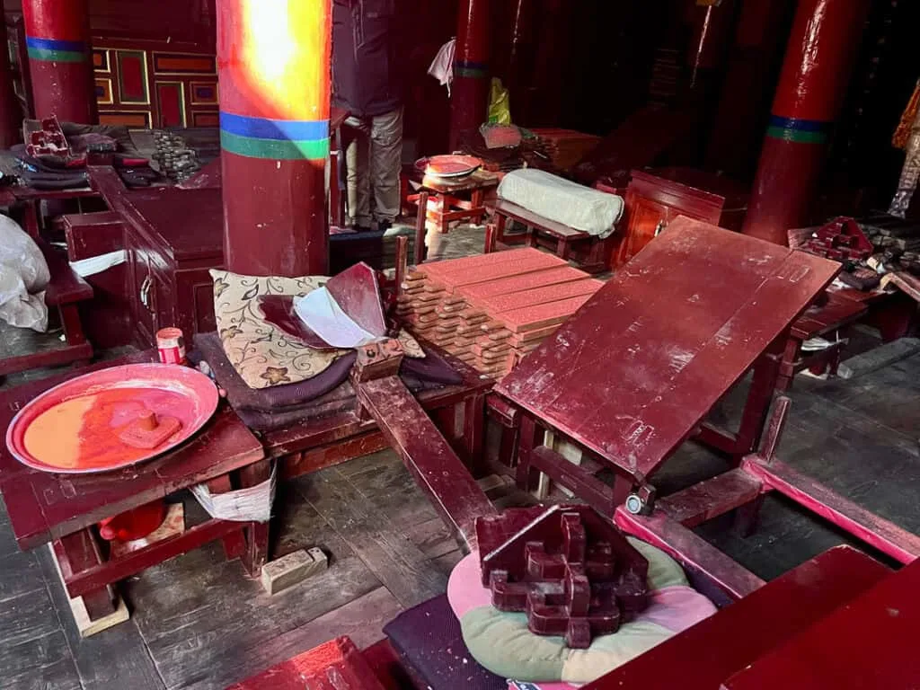 A scene from Dege Parkhang Sutra-Printing House. A bowl of red ink, wooden carved print blocks and shafts of light shining onto them from the left