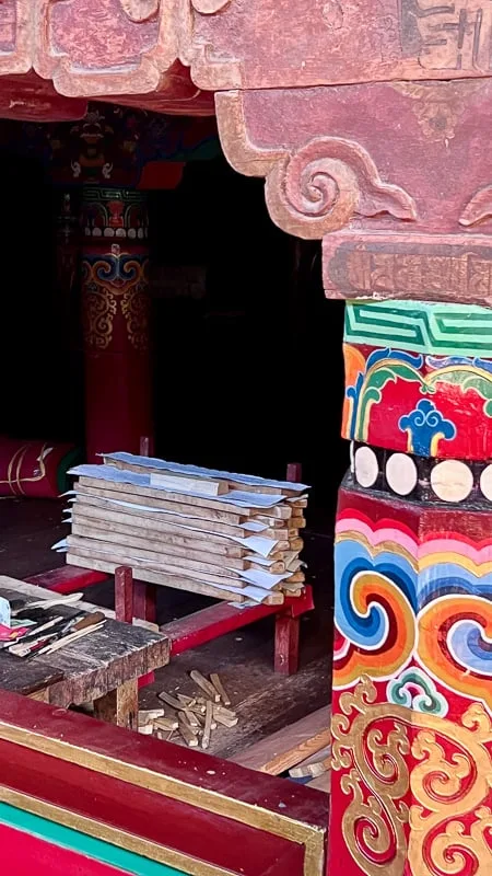 Paper drying between wooden slats in Dege Parkhang Sutra-Printing House. They are seen from outside a wooden carved doorway with painted designs on the jamb