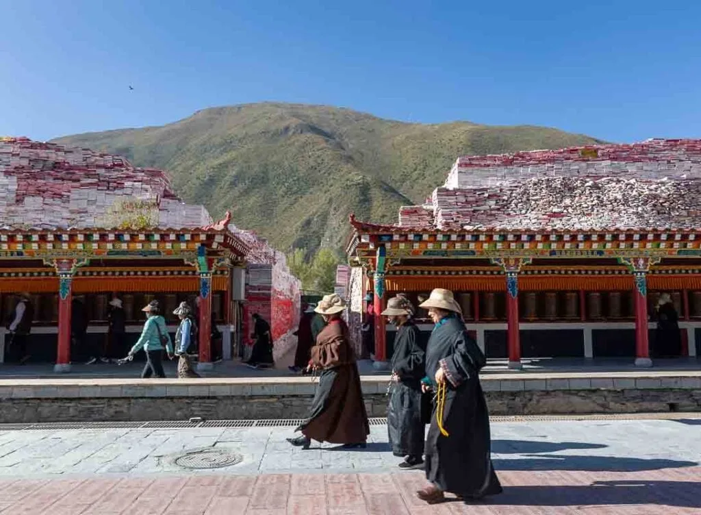 People walk past a covered terrace of prayer wheels with mani stone piles at Jiana Mani Stone City in the Tibetan Plateau.