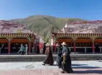 People walk past a covered terrace of prayer wheels with mani stone piles at Jiana Mani Stone City in the Tibetan Plateau.
