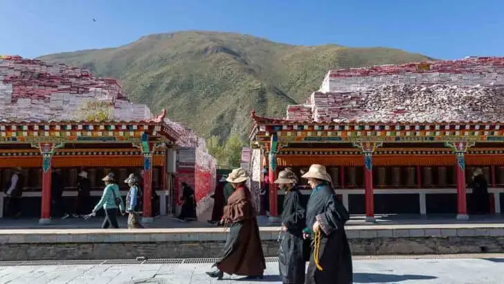 People walk past a covered terrace of prayer wheels with mani stone piles at Jiana Mani Stone City in the Tibetan Plateau.