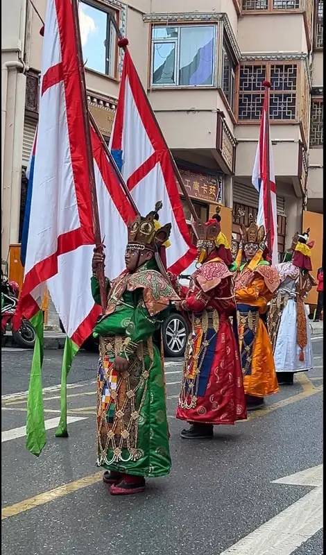 Four Tibetan monks with flags and ornate robes and headresses