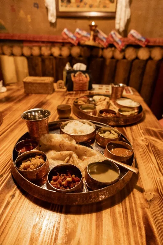 Nepalese thali meal on tray with individual dishes and chapati on a wood table