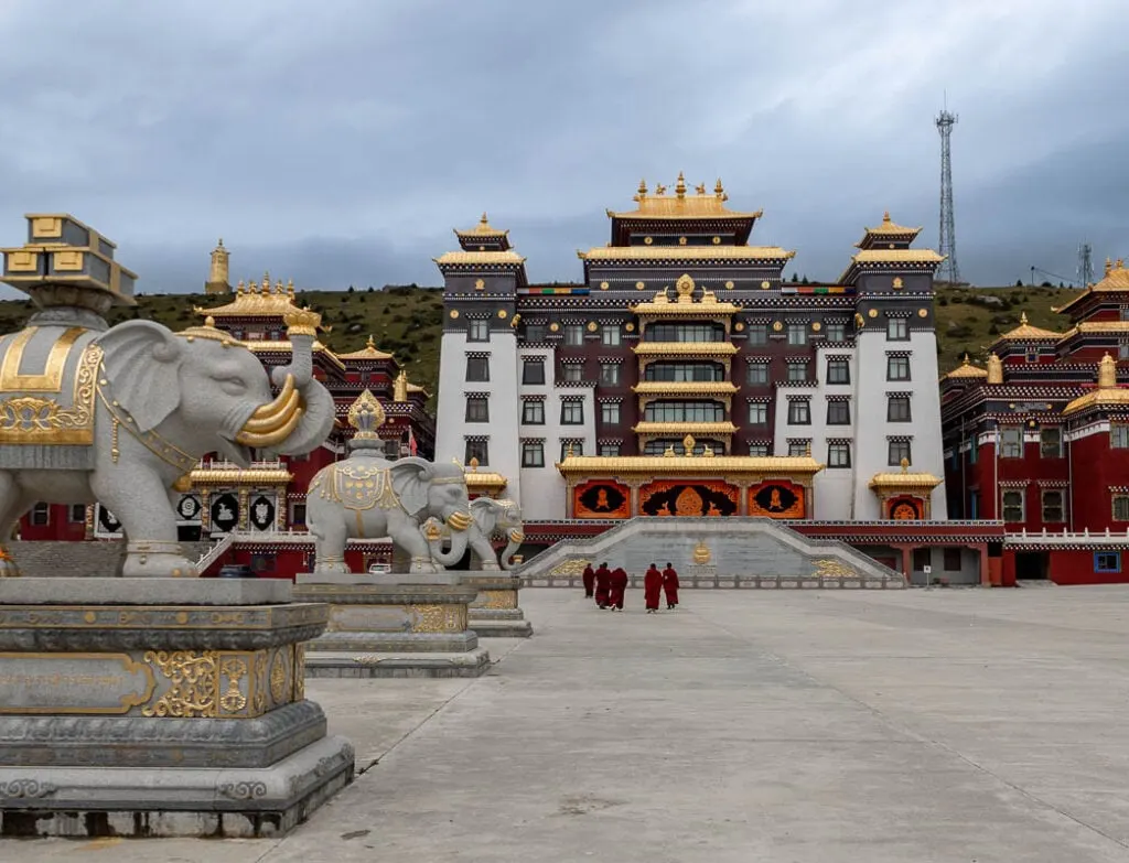 Zhuqing Monastery in Sichuan. Stone elephants on the left are embellished with gold and five monks walk towards the prayer hall in the background