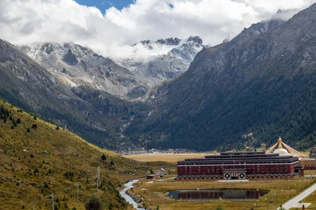 Zhuqing Monastery sits in a tree-lined valley with snow capped mountains in the background