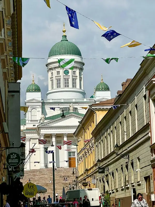Helsinki Cathedral with its white walls and green domes sits at the end of a street lined with grand apartments. Flags are strung in the foreground criss crossing across the street