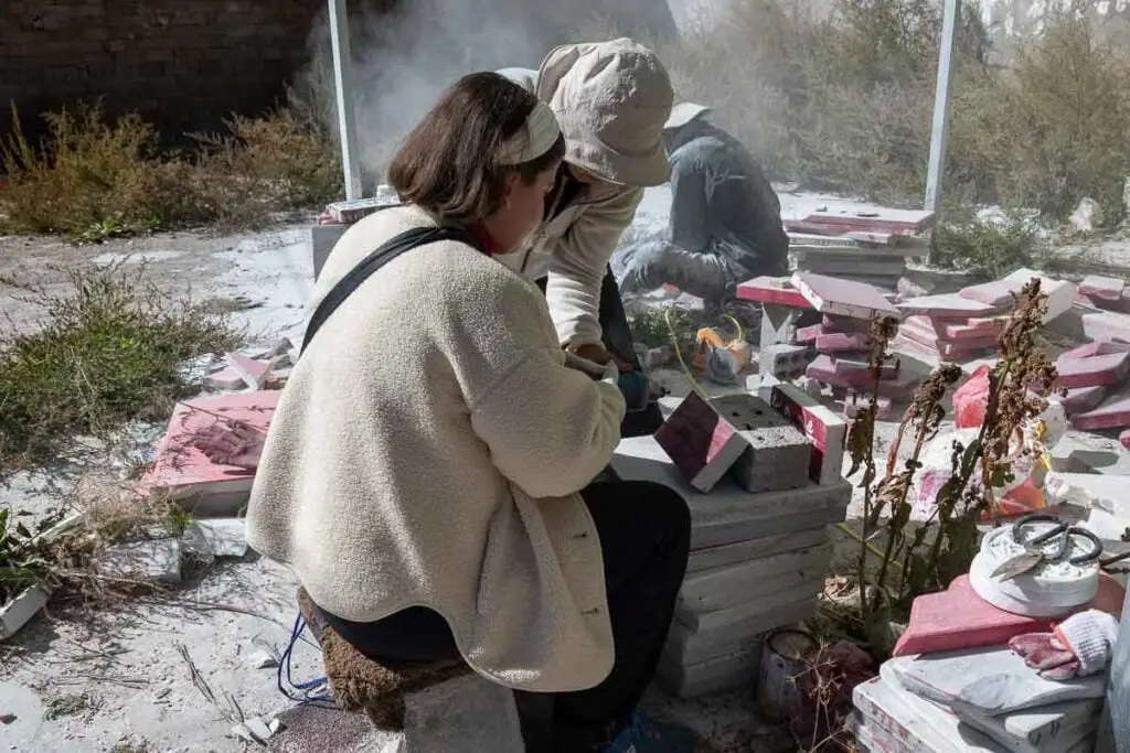 Two people carve mani stones, creating dust, at Jiana Mani Stone City on the Tibetan Plateau.