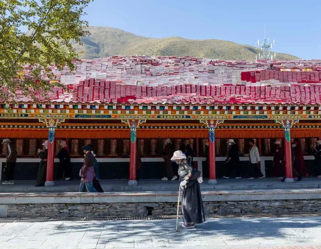 An older woman walks past prayer wheels at Jiana Mani Stone City on our China Tibetan Plateau road trip