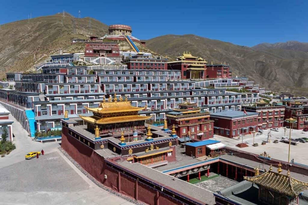 Jiegu Monastery, Yushu, China, a vast complex of traditional Tibetan buildings with golden roofs on a sunny mountain.