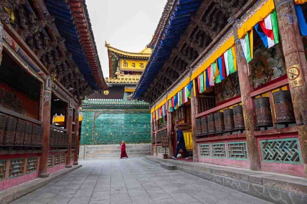 Monks in red robes prostrate and stand outside the ornate Taer Monastery.