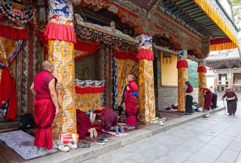 Monks in red robes prostrate and stand outside the ornate Taer Monastery.