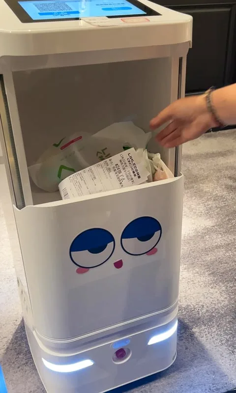 A hand reaches into a white room service robot with cartoon eyes to retrieve items in China.