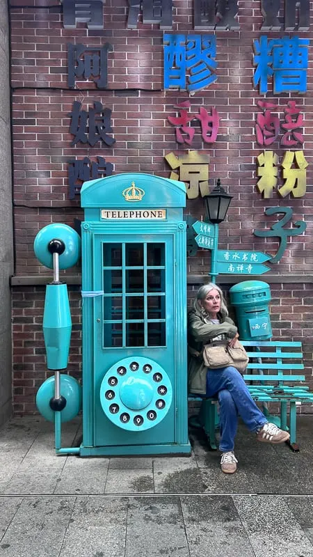 A woman sits on a teal bench next to a teal British-style telephone booth and mailbox in Xining, China.