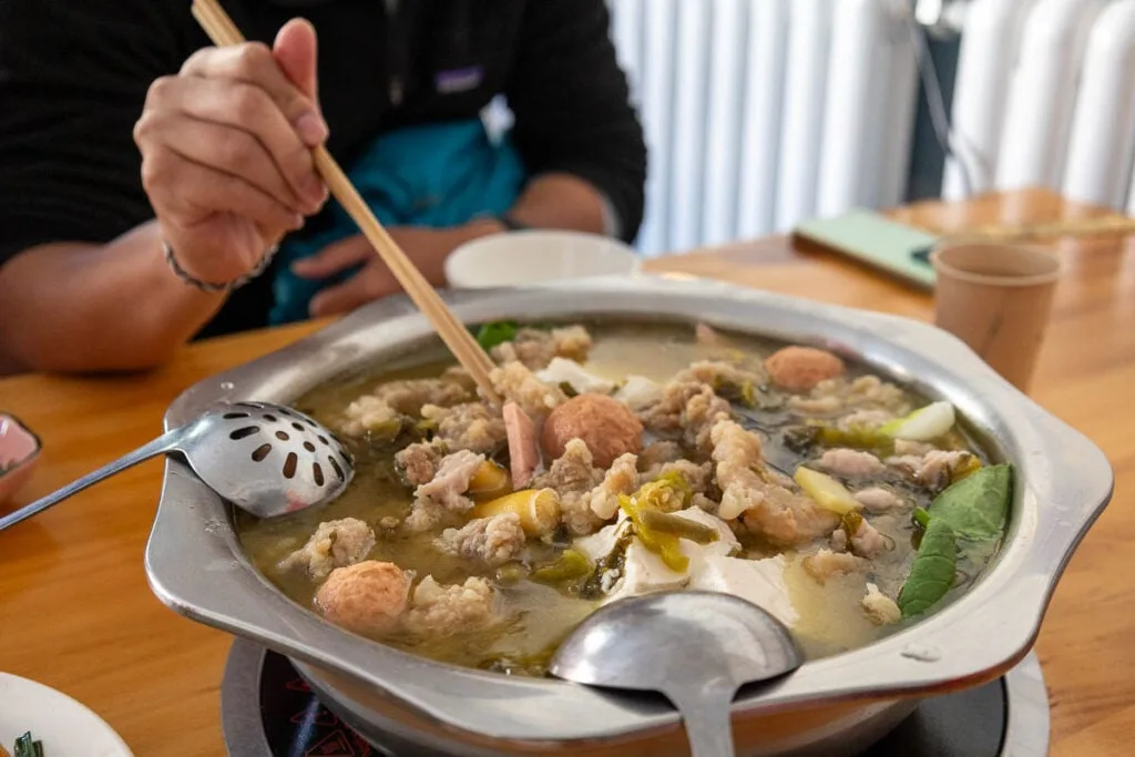 Silken tofu hot pot in Qinghai China. A hand holding chopsticks dips into the metal pot of food