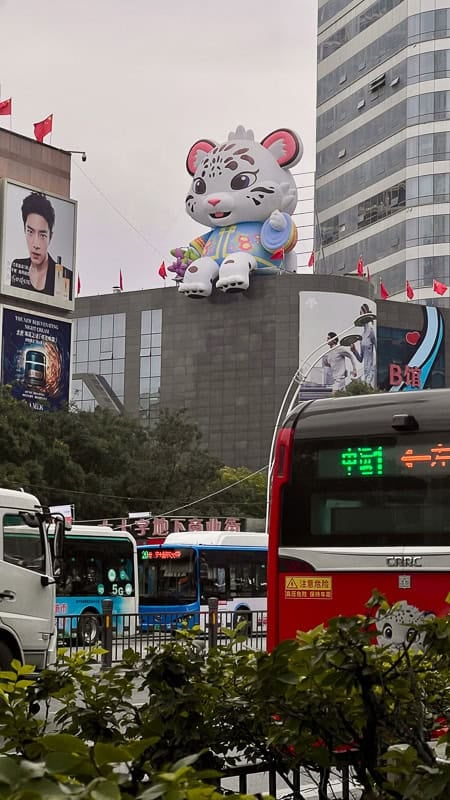 Giant snow leopard mascot on a building in Xining, Qinghai, amidst city traffic and billboards.