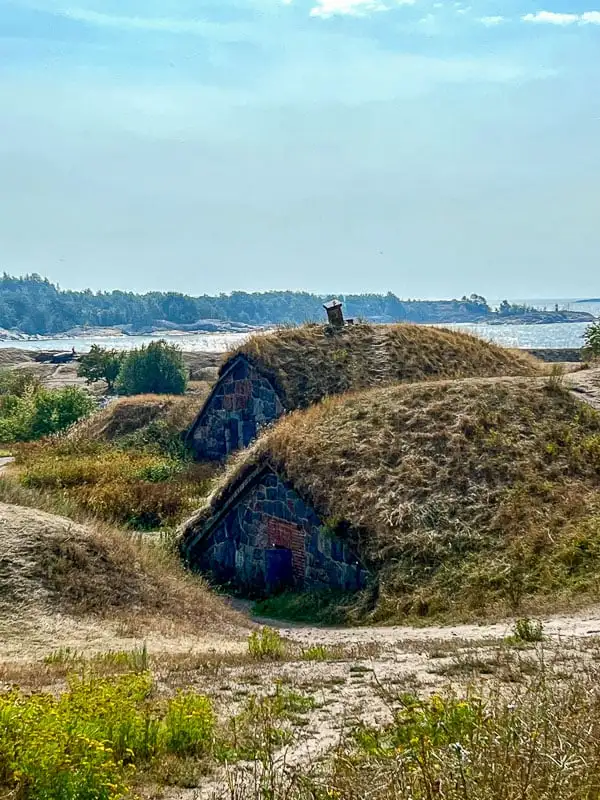 Suomenlinna Fortress small stone buildings with turfed rooftops. Trees and the sea can be seen in the background