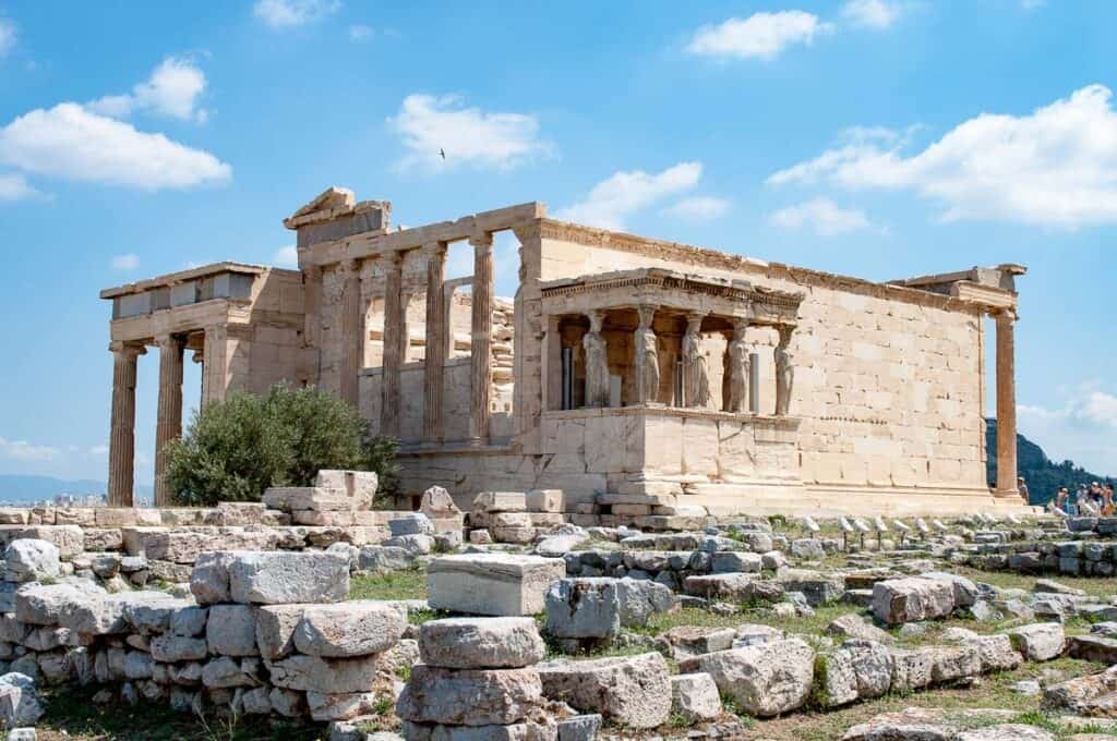 The Parthenon in Athens with old stones in the foreground and blue sky with fluffy clouds behind