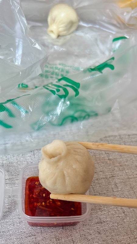 Chopsticks dip a Chinese dumpling into chili oil, with another in a bag, from Chinas Sichuan or Qinghai region.