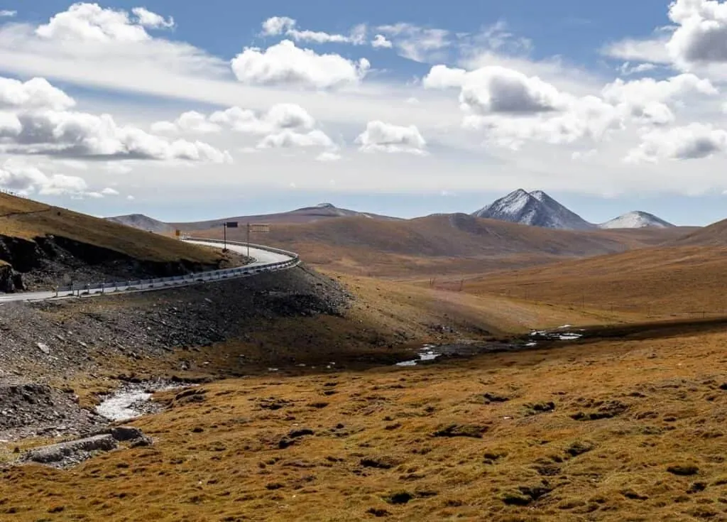 Winding road on the Tibetan Plateau from Yushu to Maduo, with golden grasslands and distant snow-capped mountains.