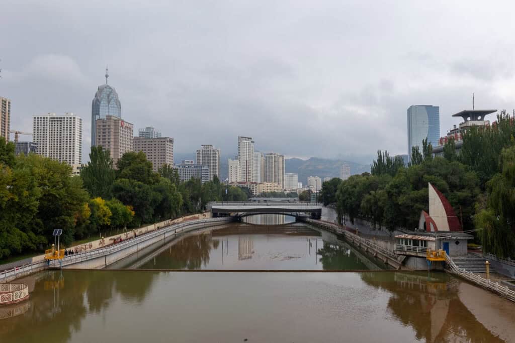 Overcast Xining cityscape with the Huangshui River, bridges, modern buildings, and distant mountains.