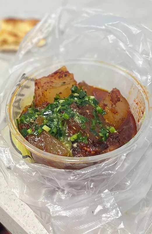 Spicy Xining night market food with jelly-like noodles and green onions in a plastic container.