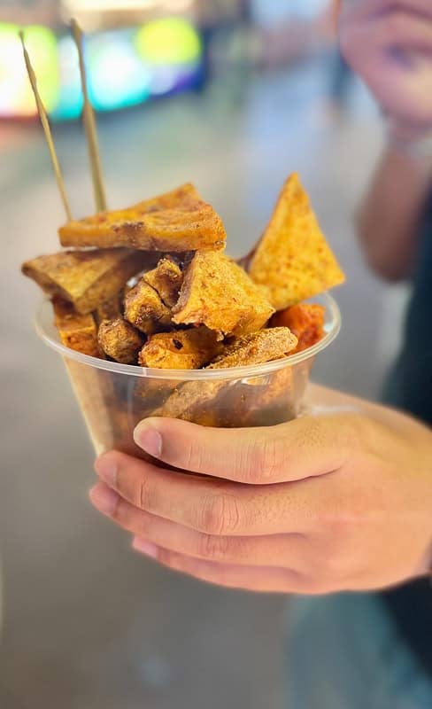 A person holds a cup of fried street food with skewers at a Xining night market.