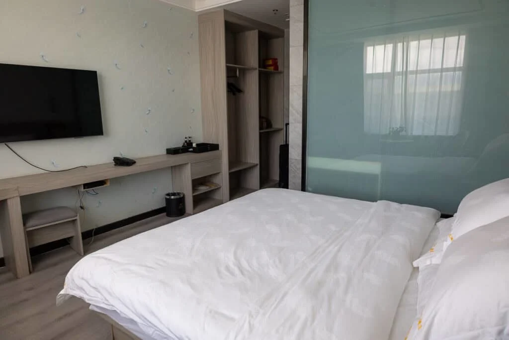 Modern hotel room at Zhaling Lake Hotel in Maduo, Qinghai, featuring a bed, wall-mounted TV, and open wardrobe.