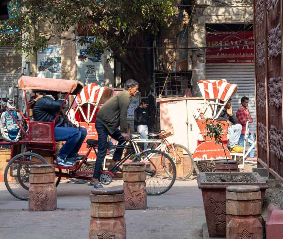 A man pedals a rickshaw past another parked rickshaw on a busy street in Chandni Chowk, Delhi.