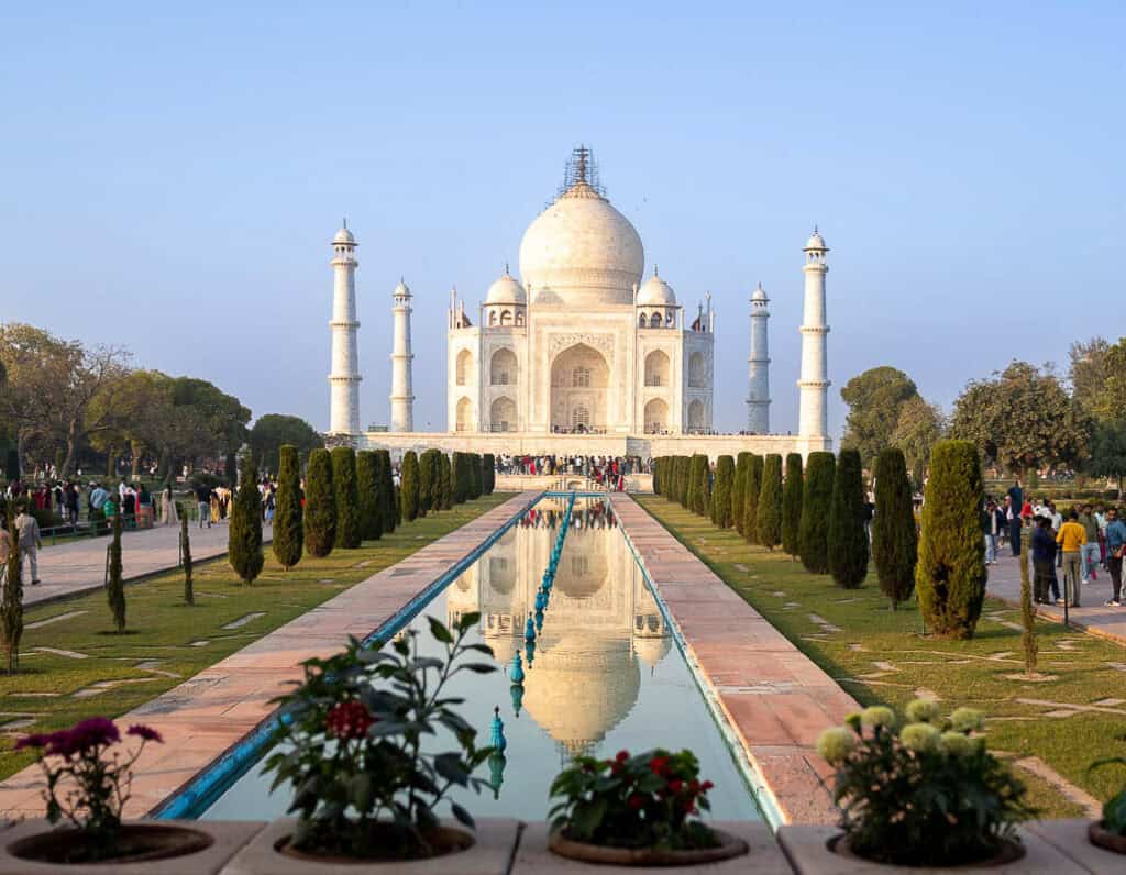 The majestic Taj Mahal in Agra, India, reflected in its tranquil pool, surrounded by lush gardens and visitors.
