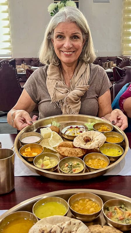 Smiling woman holding a traditional Thali meal in Varanasi, India.