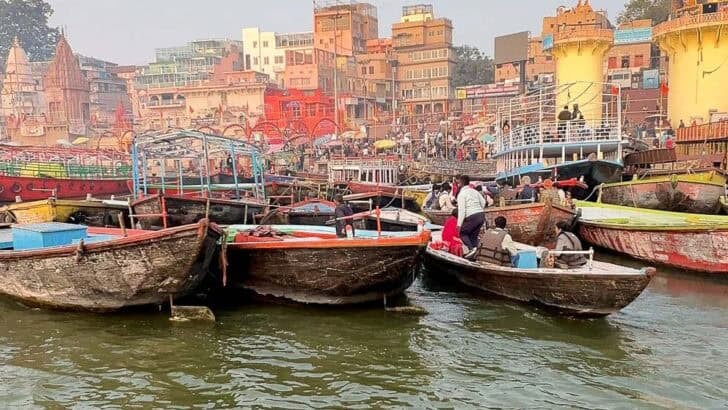 Crowded wooden boats on the Varanasi Ghats with colorful buildings lining the Ganges River.