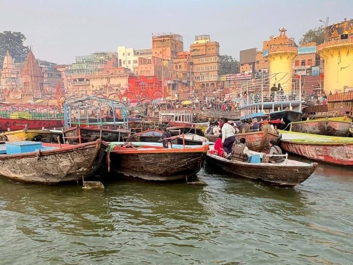 Crowded wooden boats on the Varanasi Ghats with colorful buildings lining the Ganges River.