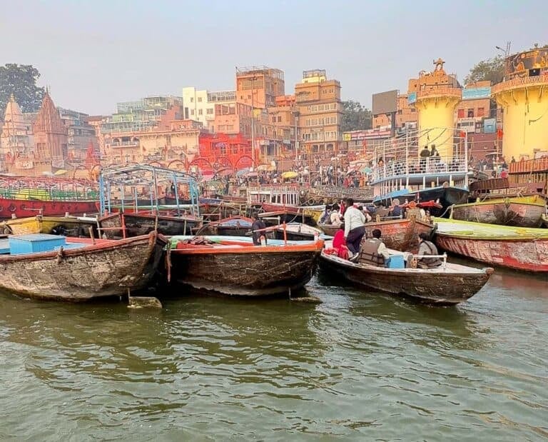 Crowded wooden boats on the Varanasi Ghats with colorful buildings lining the Ganges River.