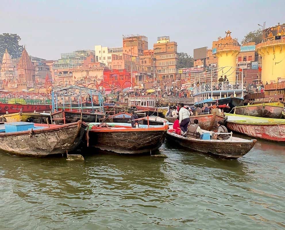 Crowded wooden boats on the Varanasi Ghats with colorful buildings lining the Ganges River.